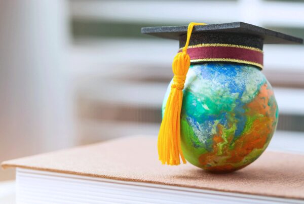A close up image of a colorful globe with a graduation cap on top of a big book